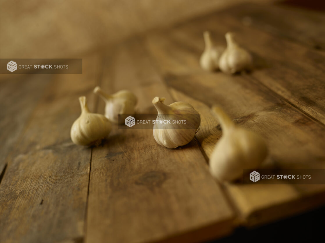 Whole garlic heads in the foreground and background on a aged wooden table