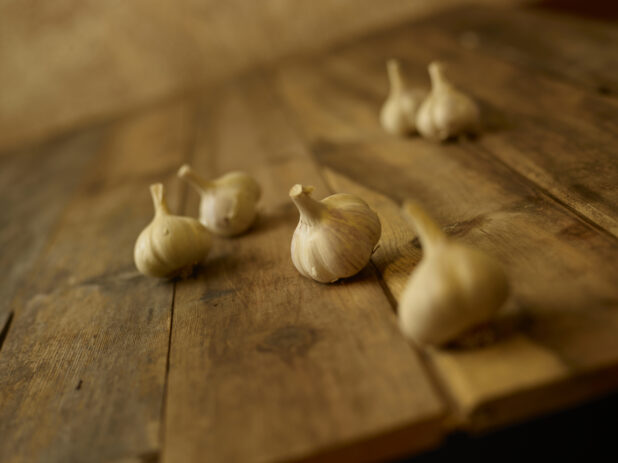Whole garlic heads in the foreground and background on a aged wooden table