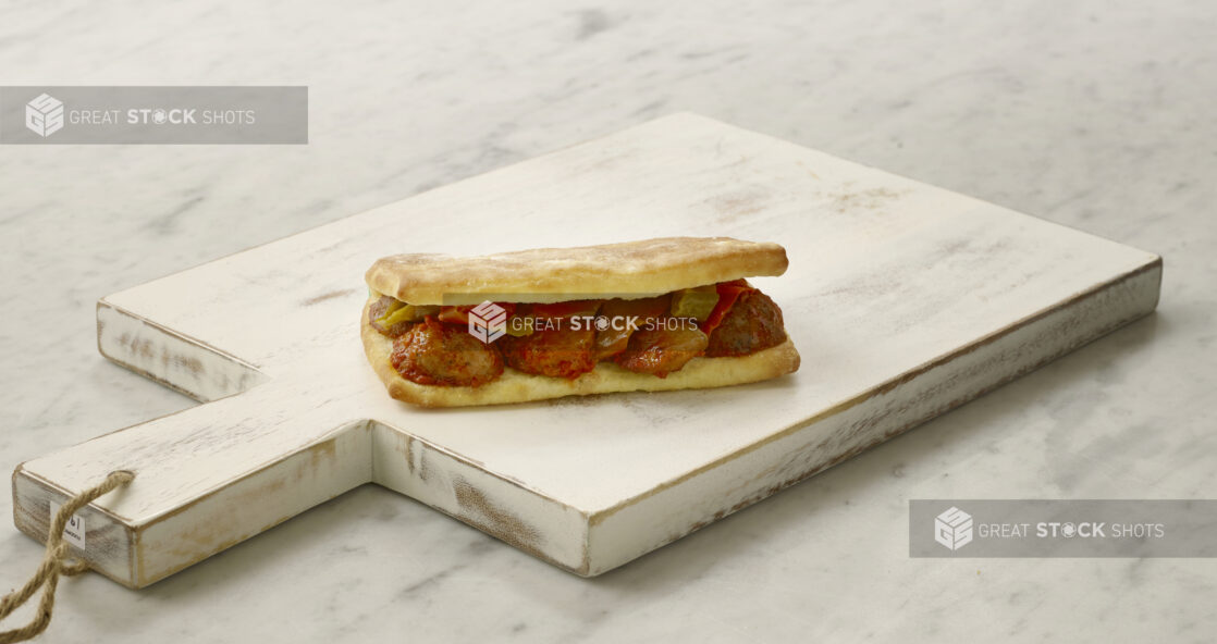 Whole meatball sandwich/hoagie on a white cutting board on a white marble table