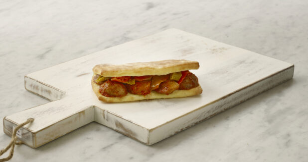 Whole meatball sandwich/hoagie on a white cutting board on a white marble table
