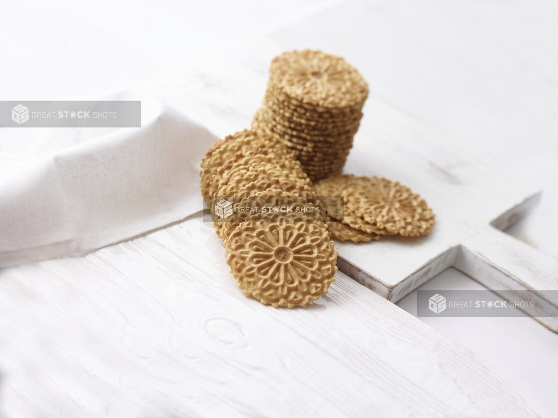 Pizzelle, Italian waffle cookies, on white wooden background, shot on an angle