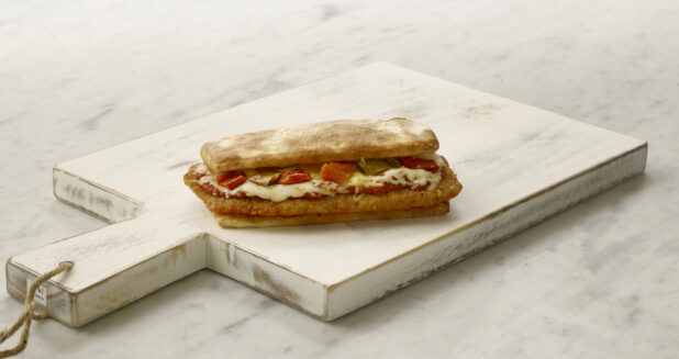 Whole chicken parmesan sandwich/hoagie with peppers on a white cutting board on a white marble table