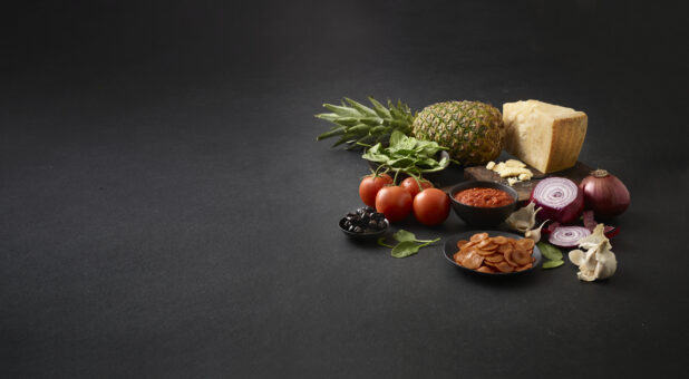 Fresh pizza toppings on a black background, shot right of centre