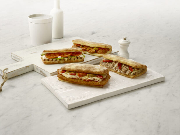 Grilled chicken, chicken parmesan, meatball and chicken shawarma sandwiches/hoagies on white cutting boards on a white marble table