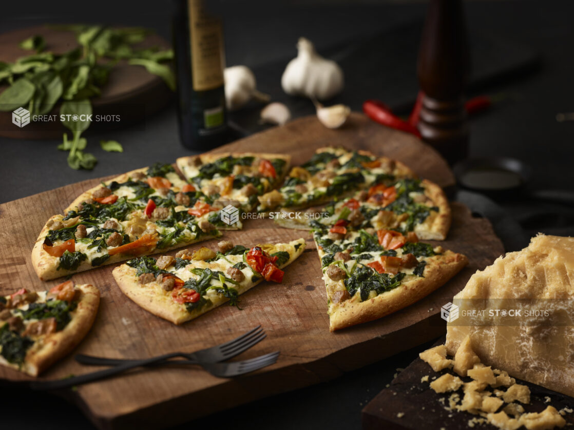 3 topping pizza on a rustic wooden board with parmesan, basil, garlic surrounding