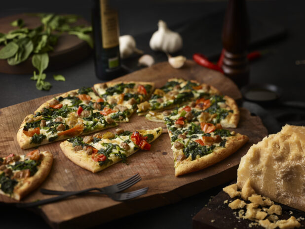 3 topping pizza on a rustic wooden board with parmesan, basil, garlic surrounding