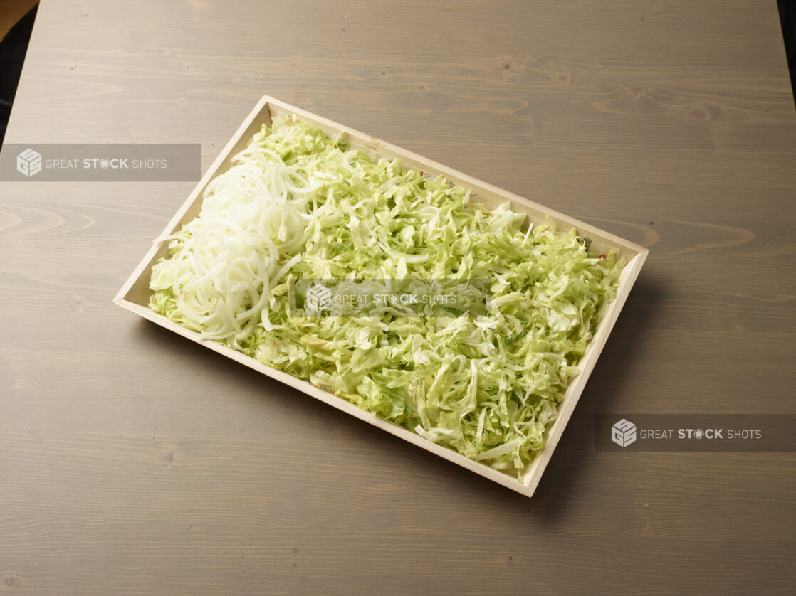 Wood catering tray filled with shredded lettuce with a pile of sliced white onions on one side, Middle Eastern platter, wood grain background