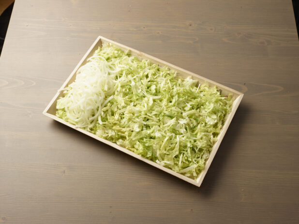 Wood catering tray filled with shredded lettuce with a pile of sliced white onions on one side, Middle Eastern platter, wood grain background