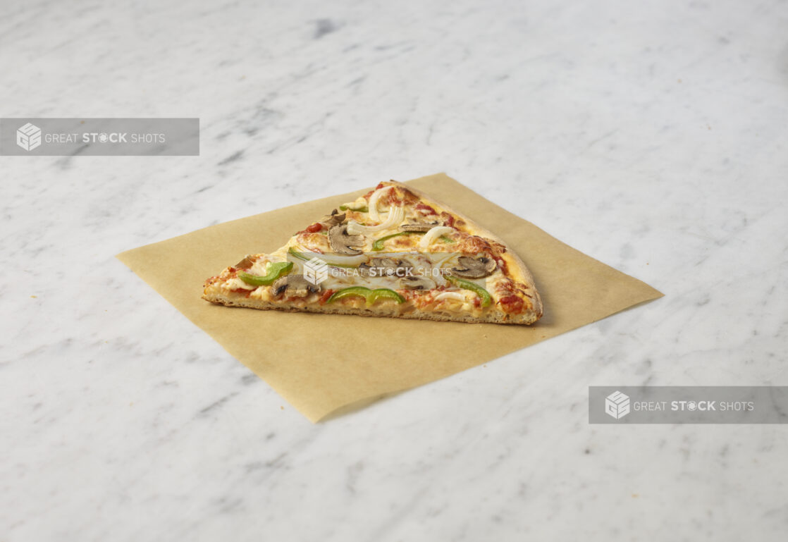 Classic Veggie Deluxe pizza slice on a square of parchment on a white marble background