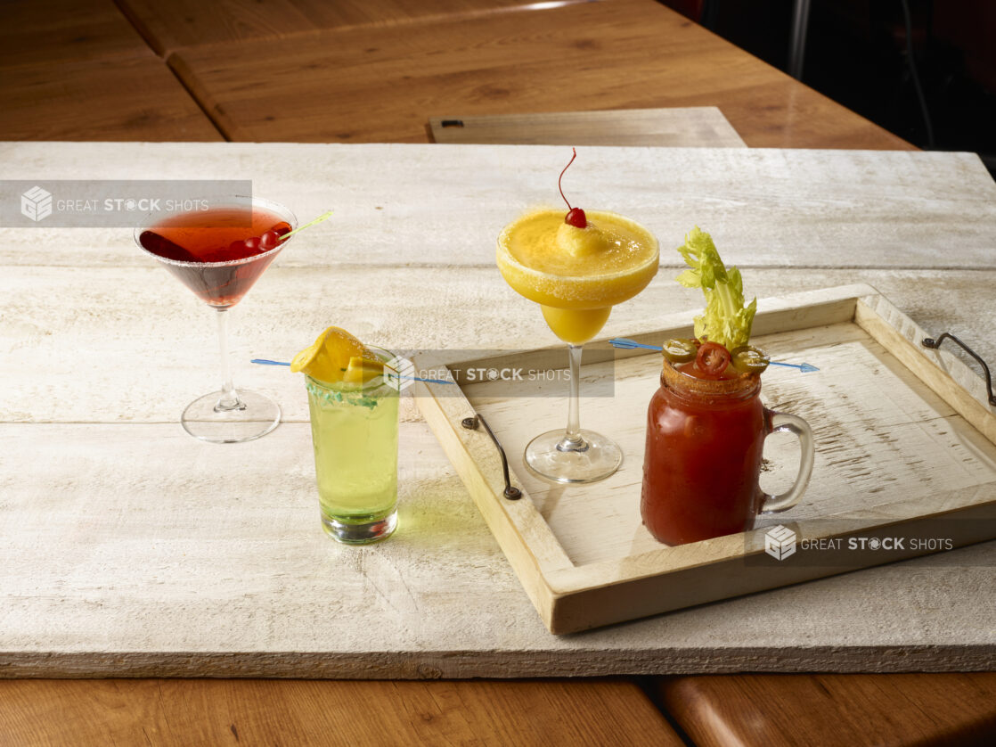 Bloody mary / caesar with tropical margarita on a wooden tray,  highball cocktail and red cocktail in a martini glass beside