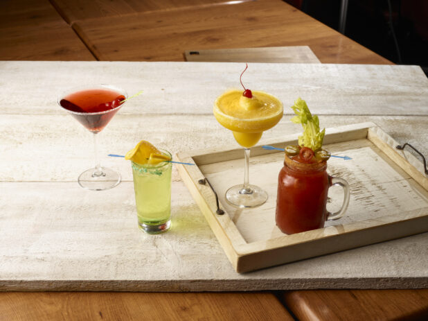 Bloody mary / caesar with tropical margarita on a wooden tray,  highball cocktail and red cocktail in a martini glass beside