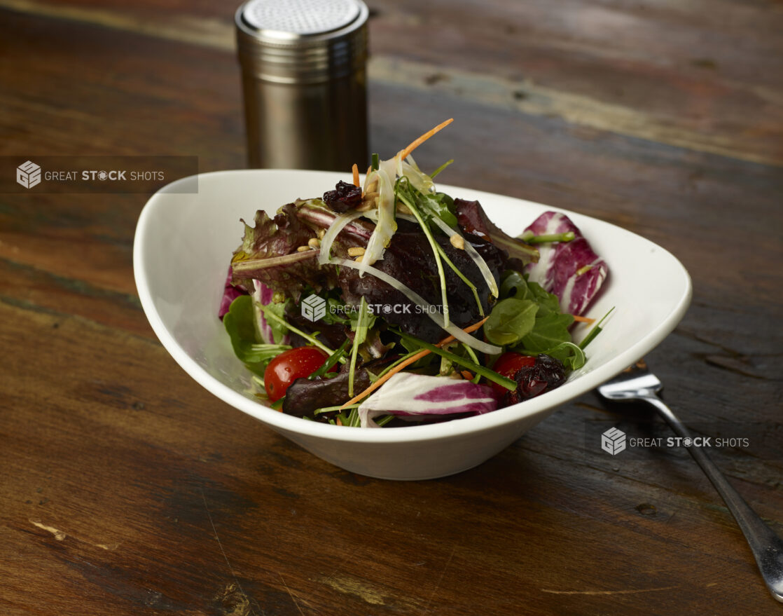 Spring mix salad in an elegant white ceramic bowl, dark wood background, close-up