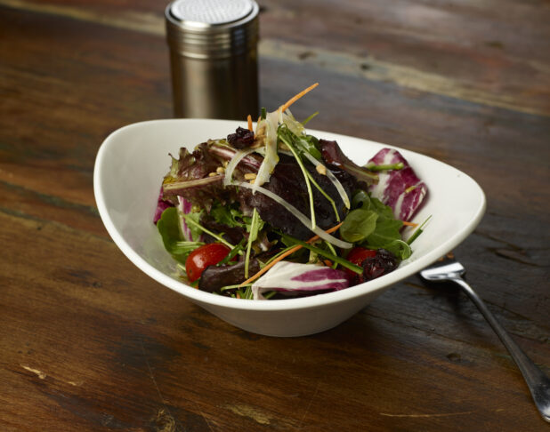 Spring mix salad in an elegant white ceramic bowl, dark wood background, close-up