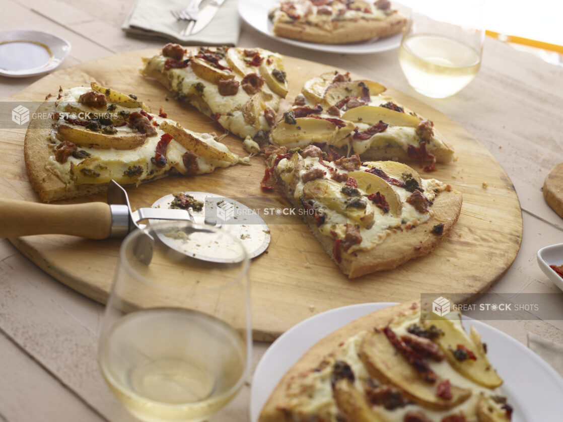 Sliced pizza with potatoes, sausage, and roasted peppers, slices removed, with pizza cutter on a round wood pizza peel