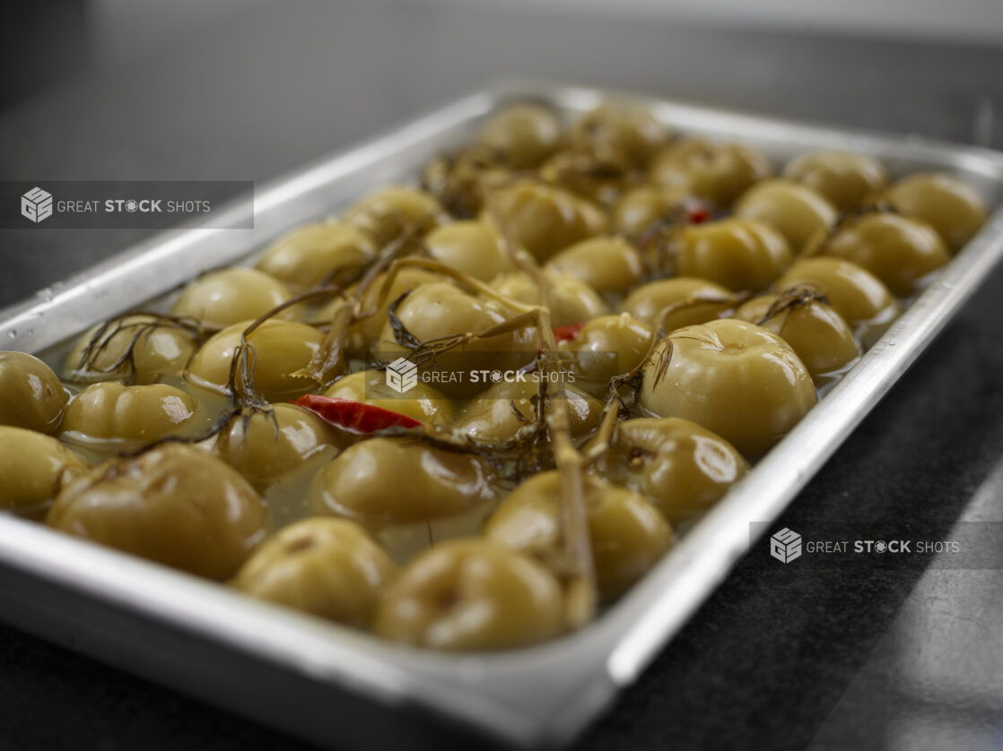 Steel insert pan of whole sour green plums in brine, close-up