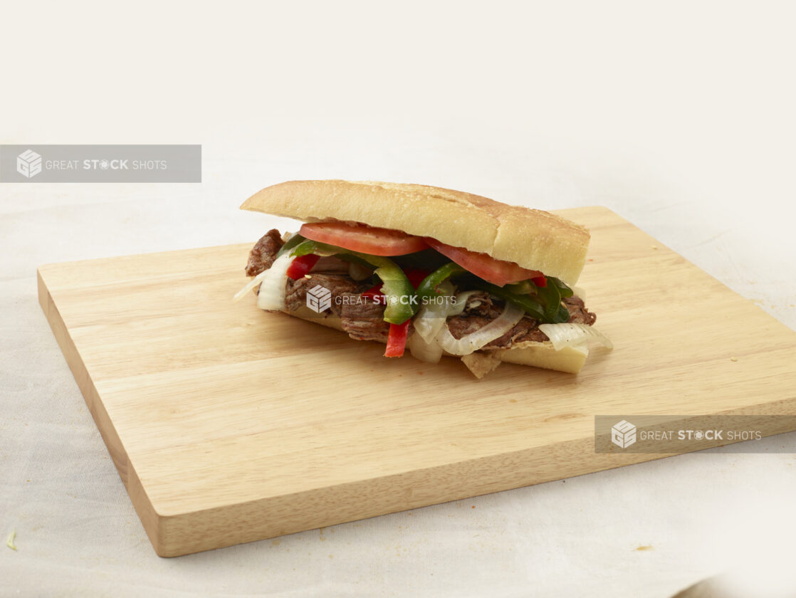 Hoagie with meat, sweet peppers and onions on a wooden cutting board