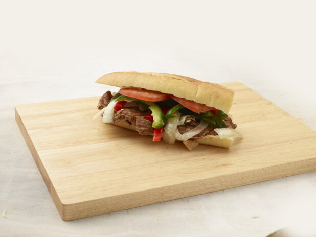 Hoagie with meat, sweet peppers and onions on a wooden cutting board