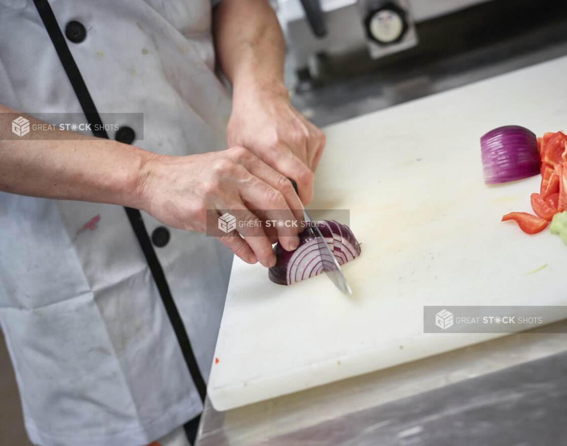 Prep cook cutting red onion on a white cutting board, kitchen setting