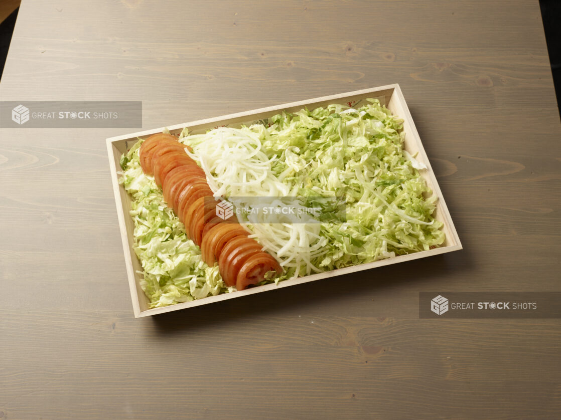 Wood catering tray filled with shredded lettuce with lines of sliced white onions and tomatoes, Middle Eastern platter, wood grain background