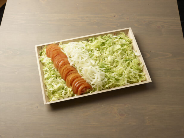 Wood catering tray filled with shredded lettuce with lines of sliced white onions and tomatoes, Middle Eastern platter, wood grain background