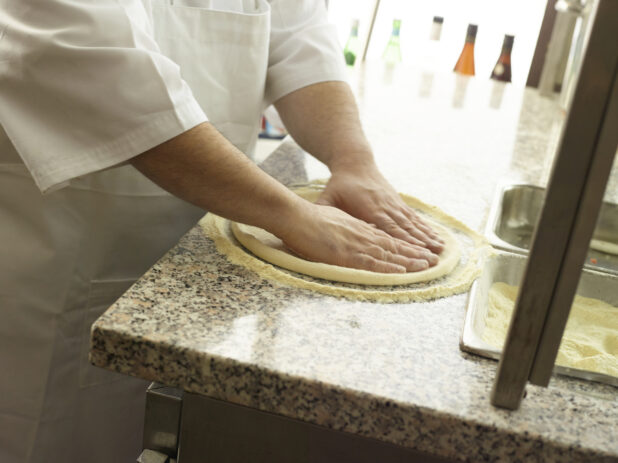 Pizza chef forming a pizza crust on a cornmeal-coated marble work surface