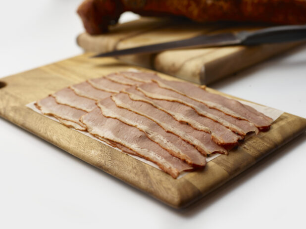 Thin slices of corned beef arranged on a wood board, background objects, white background