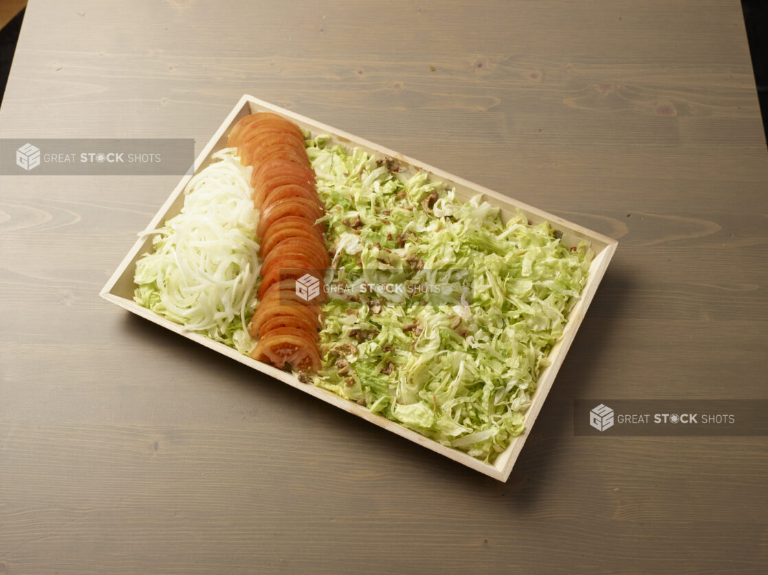 Wood catering tray filled with shredded lettuce with lines of sliced white onions and tomatoes, Middle Eastern platter, wood grain background