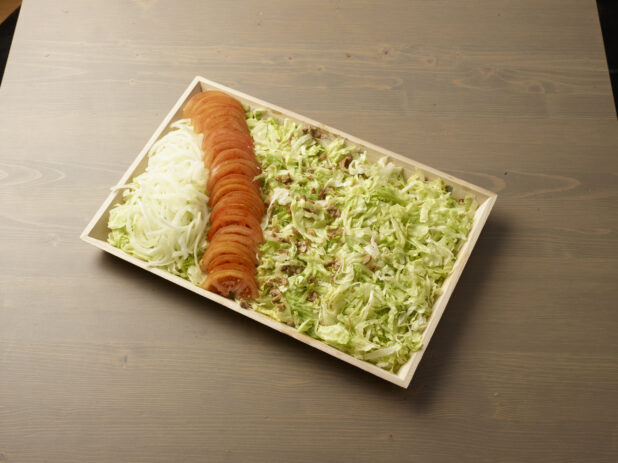 Wood catering tray filled with shredded lettuce with lines of sliced white onions and tomatoes, Middle Eastern platter, wood grain background