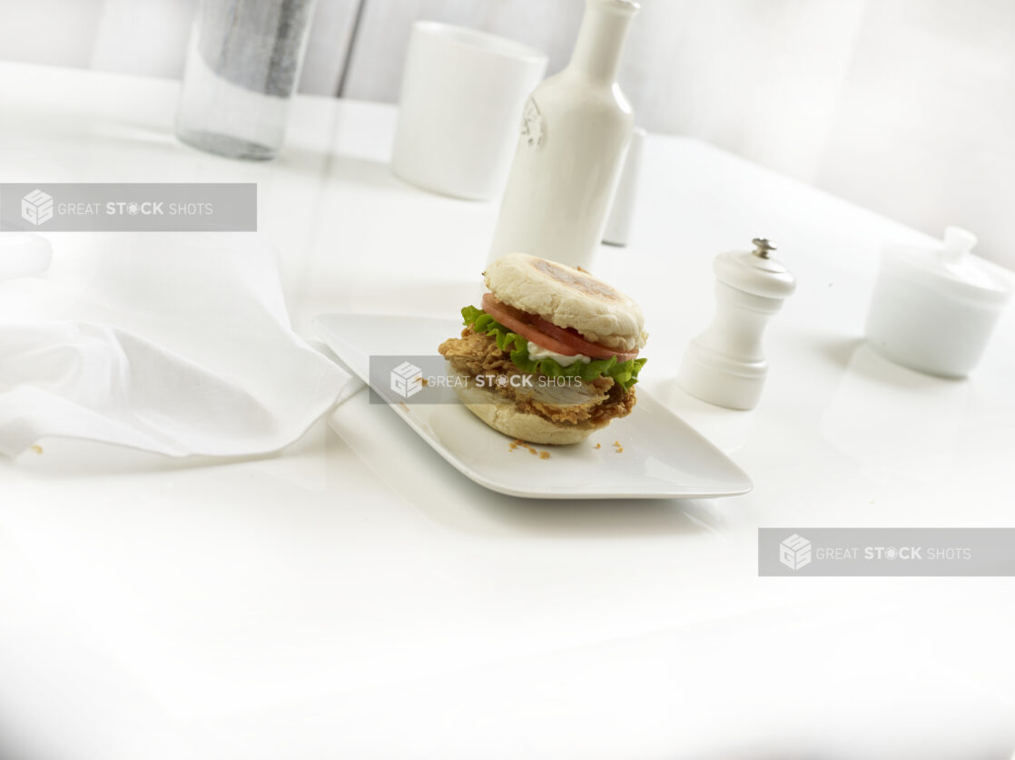 Crispy chicken breakfast sandwich on square white plate in a white table setting