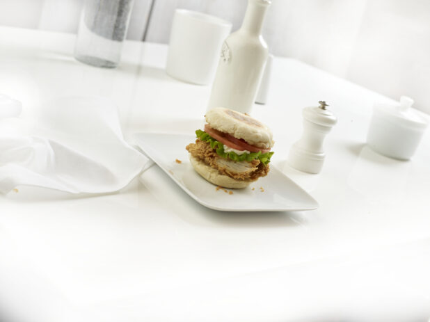 Crispy chicken breakfast sandwich on square white plate in a white table setting