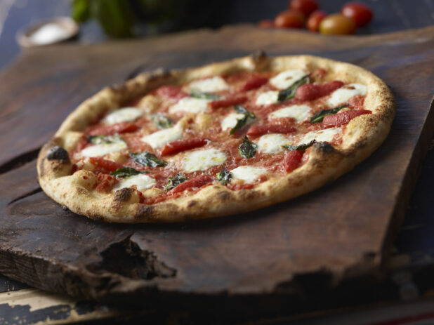 Whole Neapolitan-style Margherita pizza on a rustic wood background, tilted angle