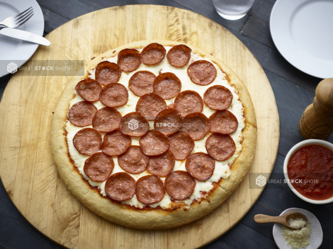 Whole pepperoni pizza on a round wood board, overhead