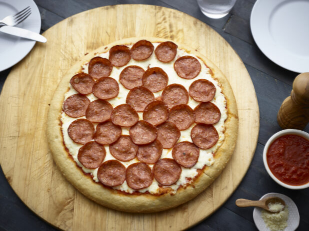 Whole pepperoni pizza on a round wood board, overhead