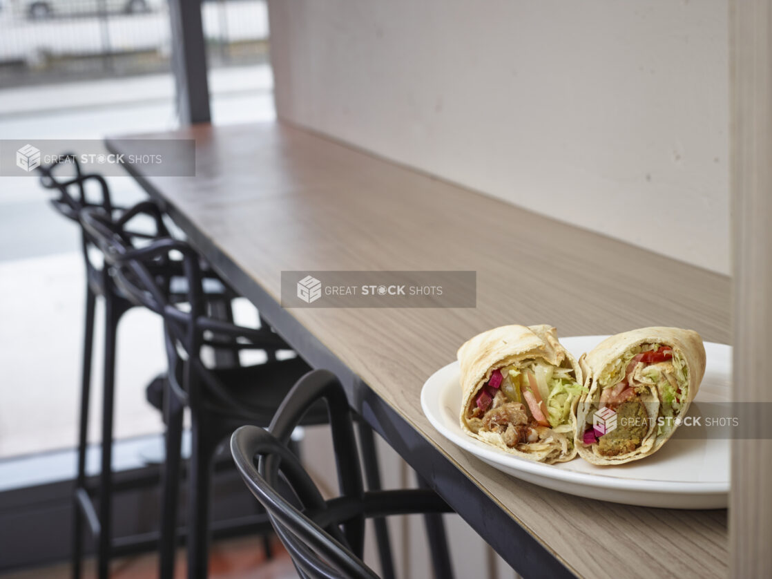 Middle eastern shawarma and falafel pita on a plate sitting on top of a wooden table in a restaurant