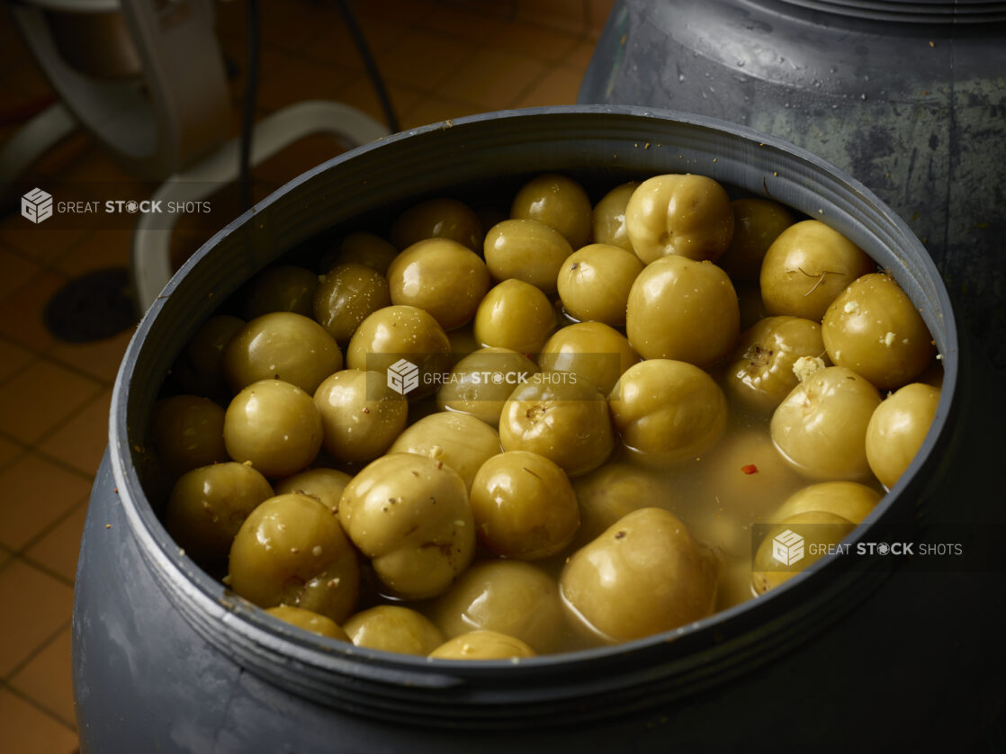 Pickled green plums in brine in a black vat, close-up