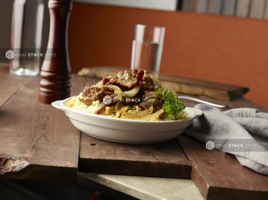 Steak and eggs on rice with sautéed onions in a white ceramic bowl, close-up, low angle