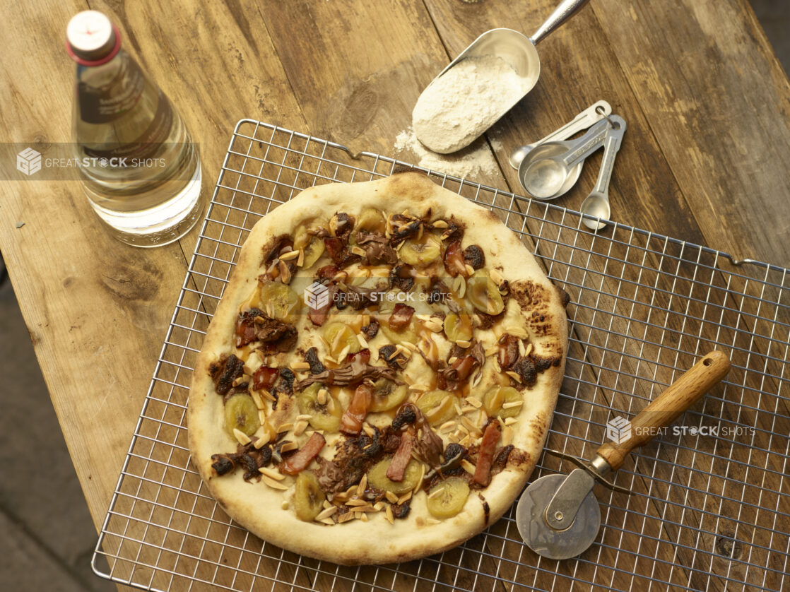 Dessert pizza on a wire cooling rack with pizza cutter, wood background