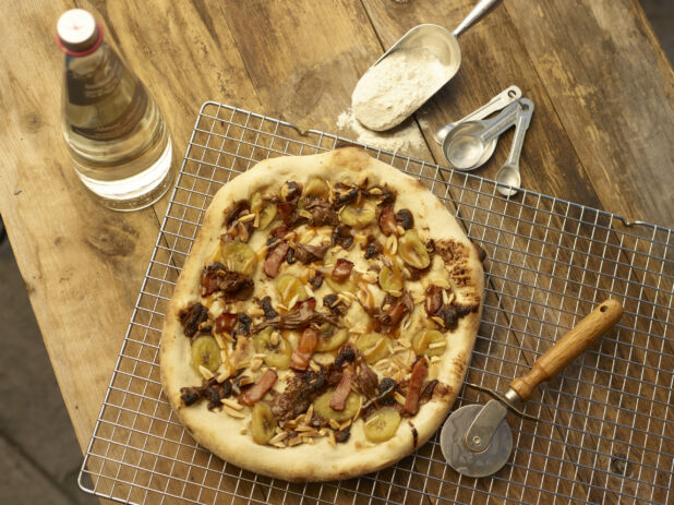 Dessert pizza on a wire cooling rack with pizza cutter, wood background