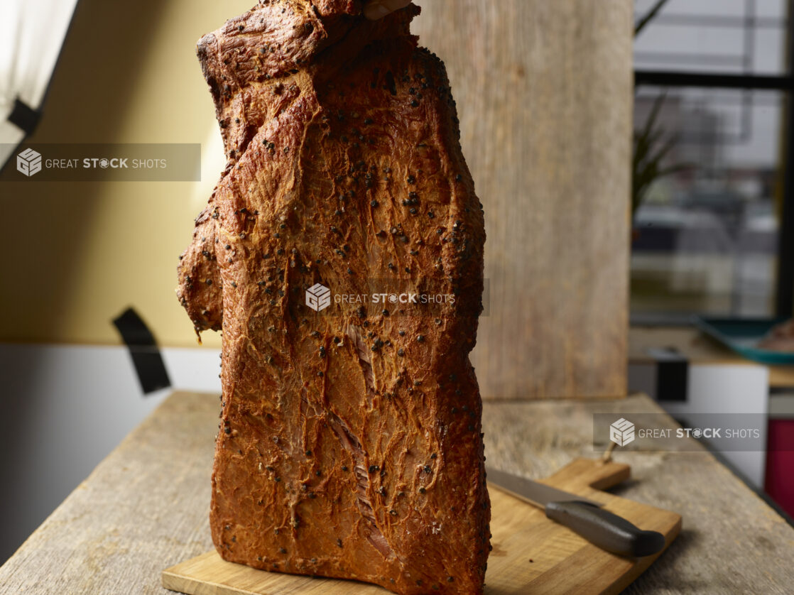 Whole pastrami upright on a wood board, close-up