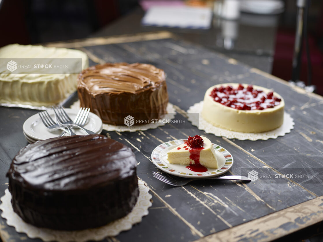 Various cakes - chocolate iced, cherry cheesecake, vanilla iced - on a dark weathered wood tabletop