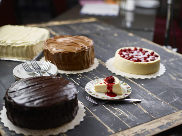 Various cakes - chocolate iced, cherry cheesecake, vanilla iced - on a dark weathered wood tabletop