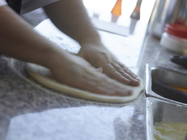 Pizza chef forming dough into a pizza crust on a cornmeal-dusted marble work surface