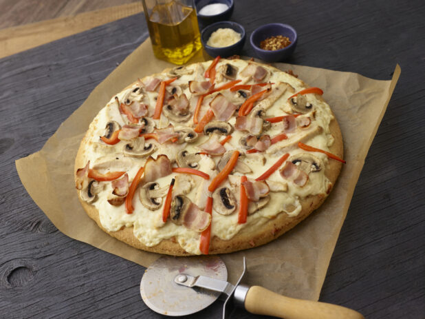 Whole white pizza with mushrooms, red peppers, chicken, bacon and cheese on dark wooden background