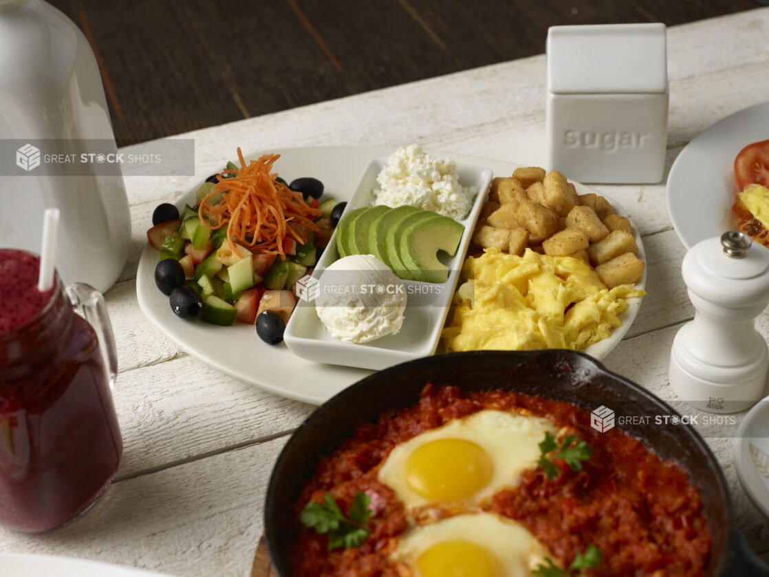 Breakfast table with various dishes including shakshouka and dairy breakfast plate, white table setting