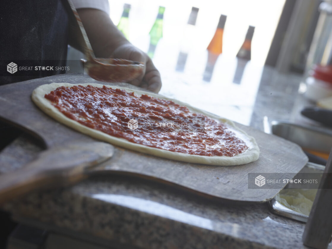 Pizza chef spreading tomato sauce around pizza dough on a peel in a restaurant