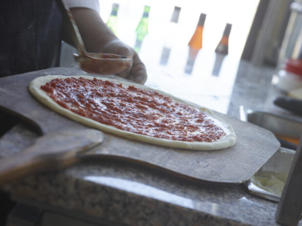 Pizza chef spreading tomato sauce around pizza dough on a peel in a restaurant