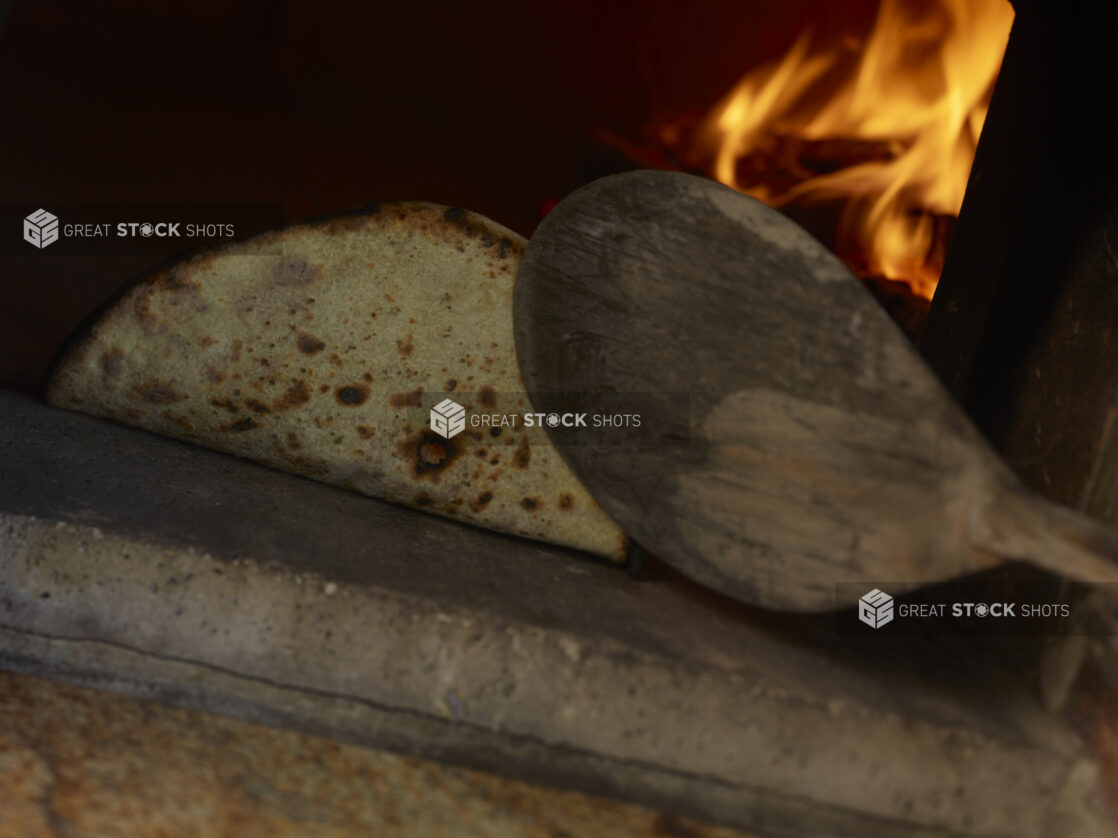 Flatbread Being Fire-Baked in a Wood-Burning Oven and Flipped with a Wooden Paddle