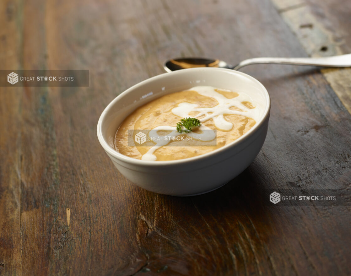 Bowl of creamy squash soup with cream drizzle and garnish on a wooden table