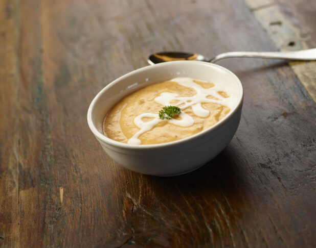 Bowl of creamy squash soup with cream drizzle and garnish on a wooden table