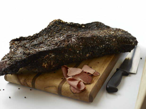 Whole Smoked Beef Brisket on a Wooden Cutting Board with Some Slices in a Kitchen Setting